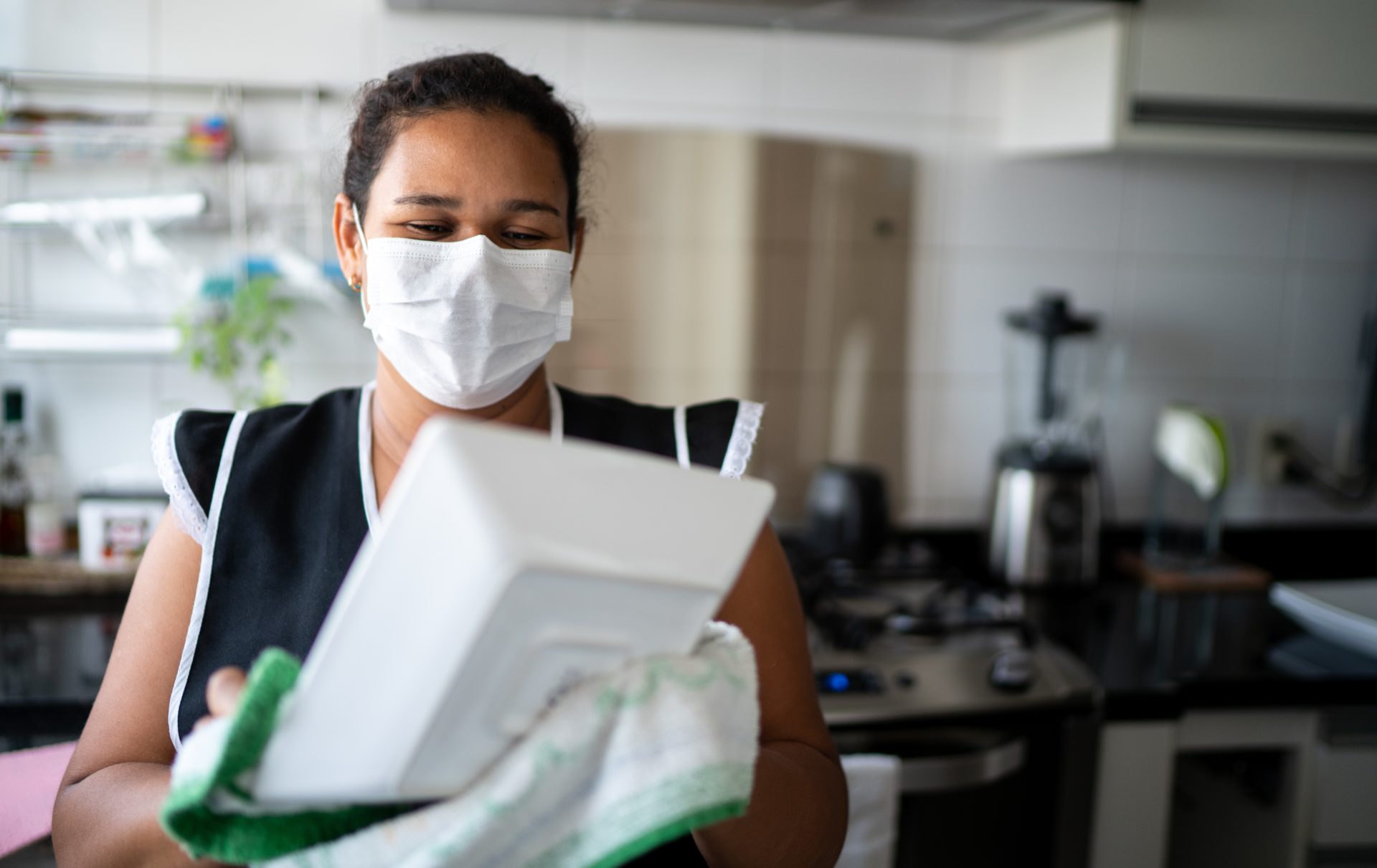 Housekeeper washing the dishes wearing protective mask