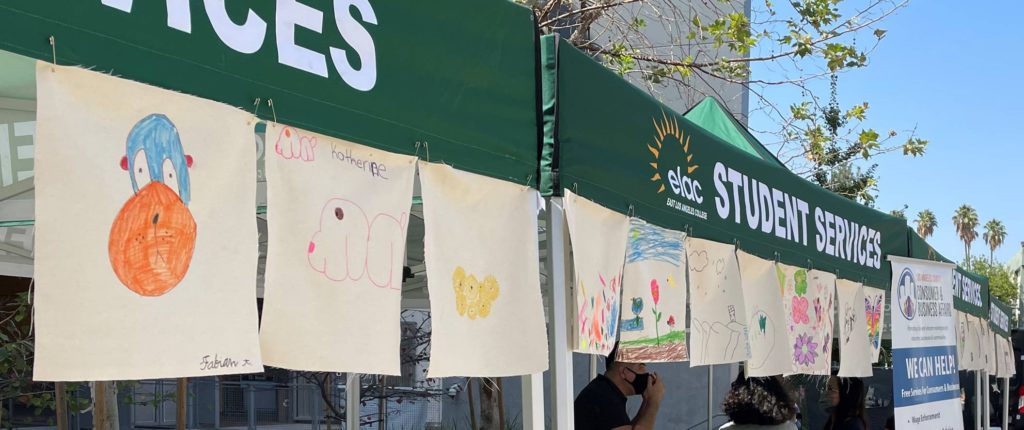 Children's artwork hangs from portable booths at a community event.